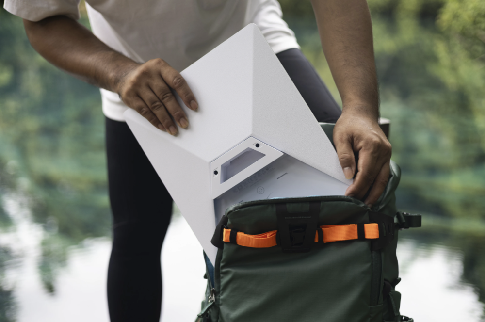 Persona guardando una antena Starlink de color blanco en una mochila verde en un entorno natural.