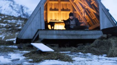 Antena parabólica rectangular de Starlink instalada en un terreno con nieve frente a una cabaña de madera.