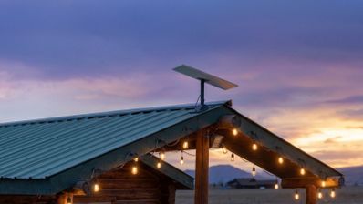 Antena parabólica rectangular de Starlink instalada en el tejado de una cabaña de madera al atardecer.