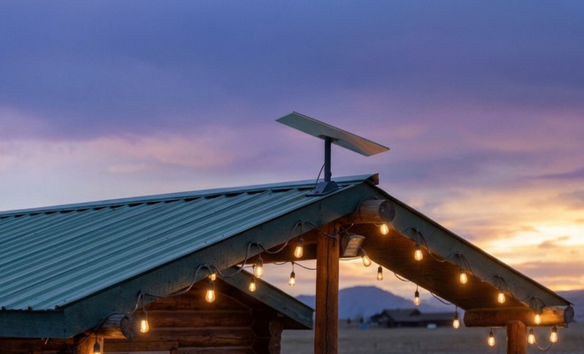 Antena parabólica rectangular de Starlink instalada en el tejado de una cabaña de madera al atardecer.