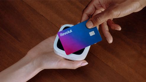 Persona realizando un pago con tarjeta Revolut en un datáfono inalámbrico sobre una mesa de madera.