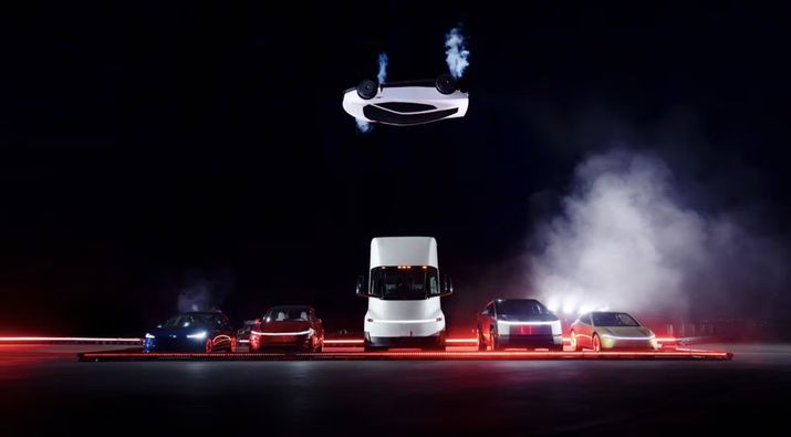 Vehículos Tesla estacionados en línea con un Tesla Roadster flotando encima bajo una luz tenue.