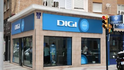 Fachada de una tienda DIGI Store en la esquina de una calle urbana con cartelería azul corporativa.