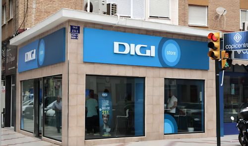 Fachada de una tienda DIGI Store en la esquina de una calle urbana con cartelería azul corporativa.