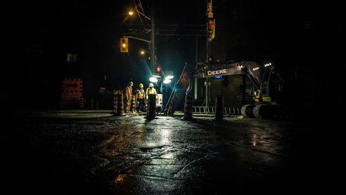Operarios realizando tareas de mantenimiento en una calle durante la noche bajo focos de luz blanca.