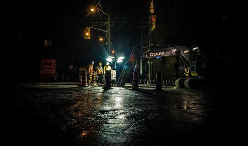 Operarios realizando tareas de mantenimiento en una calle durante la noche bajo focos de luz blanca.