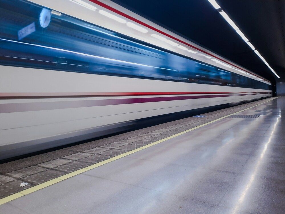 Tren de pasajeros pasando a gran velocidad por el andén de una estación subterránea.