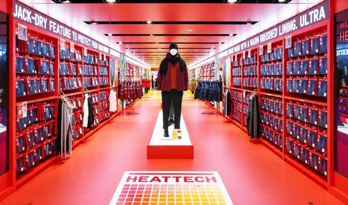 Interior de una tienda Uniqlo con pasillo central rodeado de estanterías rojas y productos Heattech.
