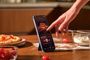 Mano interactuando con la pantalla de un xiaomi-note-17 que reproduce música en una cocina.