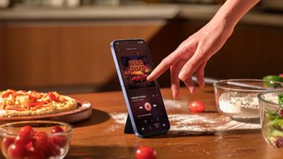 Mano interactuando con la pantalla de un xiaomi-note-17 que reproduce música en una cocina.