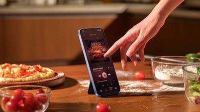 Mano interactuando con la pantalla de un xiaomi-note-17 que reproduce música en una cocina.