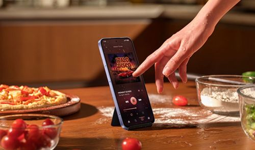 Mano interactuando con la pantalla de un xiaomi-note-17 que reproduce música en una cocina.