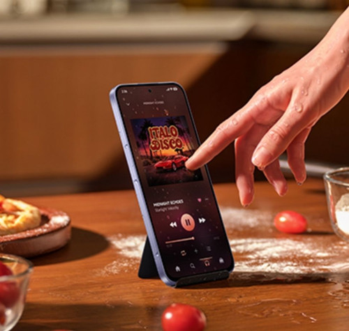Mano interactuando con la pantalla de un xiaomi-note-17 que reproduce música en una cocina.